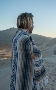 Young man standing on sand dunes contemplating beautiful landscape at sunset