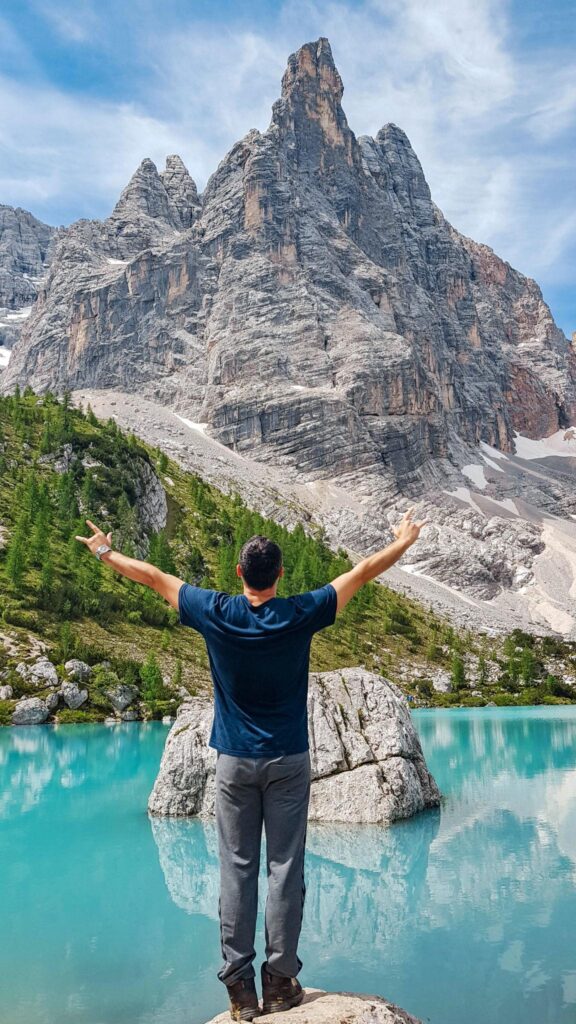 Person standing on a rock with open arms near a crystal clear lake under the sunlight