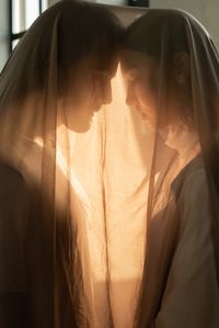 Intimate portrait of a couple under a sheer veil, creating a warm, romantic feel.