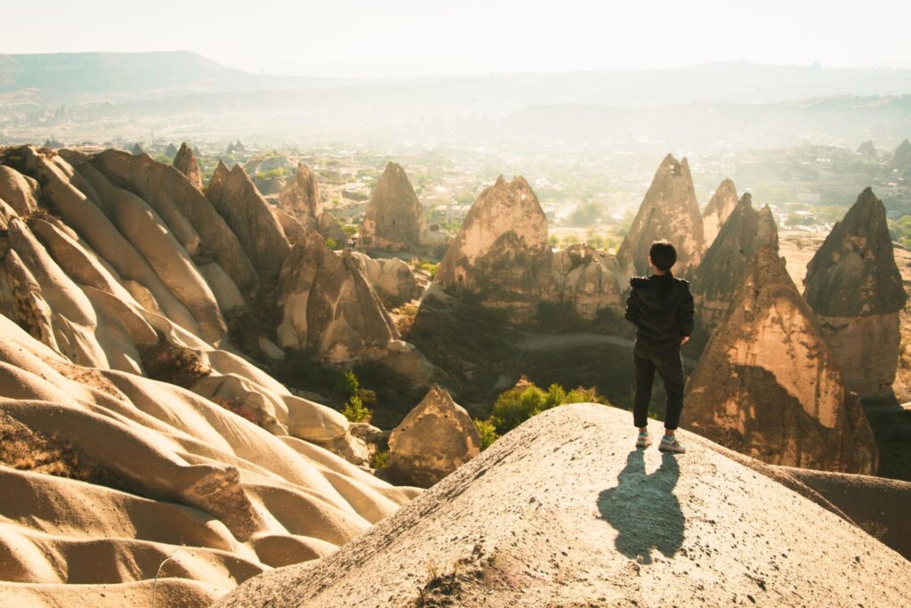 Thoughtful Female person stand look over dramatic valley on hazy morning sunrise with fairy chimneys background. Solo exploration in Turkey